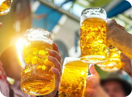 太陽光が差し込む中で大勢がビールジョッキを掲げて乾杯しているイメージ